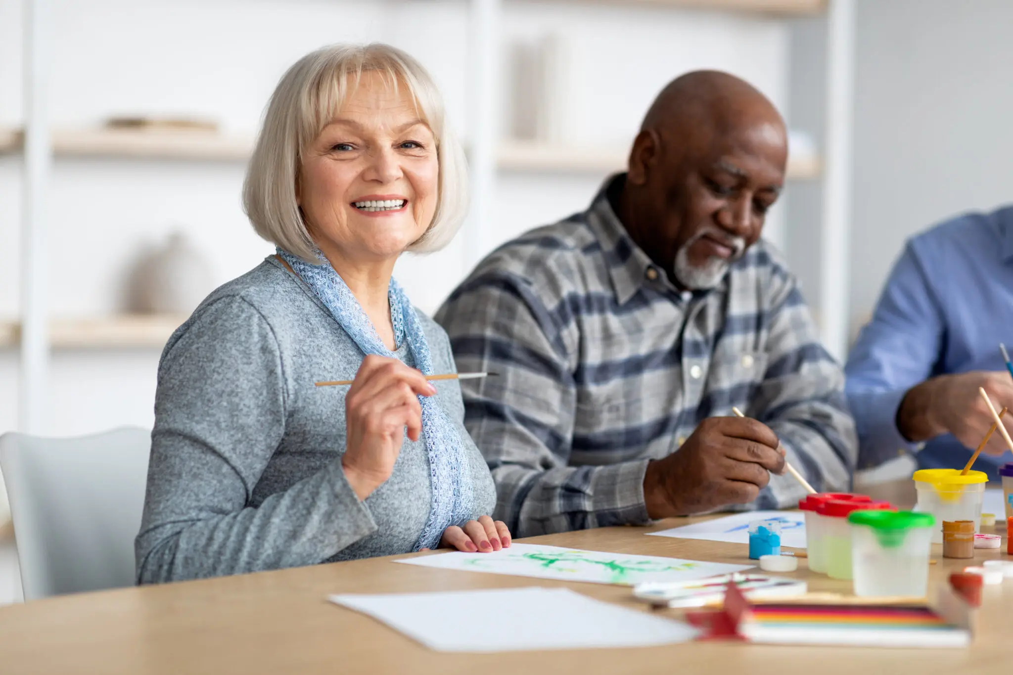 Positive senior woman enjoying painting with brush Art-therapy for seniors concept. Positive multiracial group of elderly people enjoying painting with brush, sitting around table, having good time together at assisted lliving, closeup photo